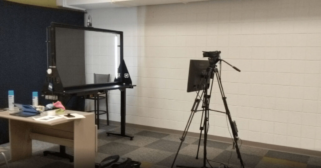 Lightboard classroom setup with glass board, lighting equipment, and desk supplies in a Providence College room